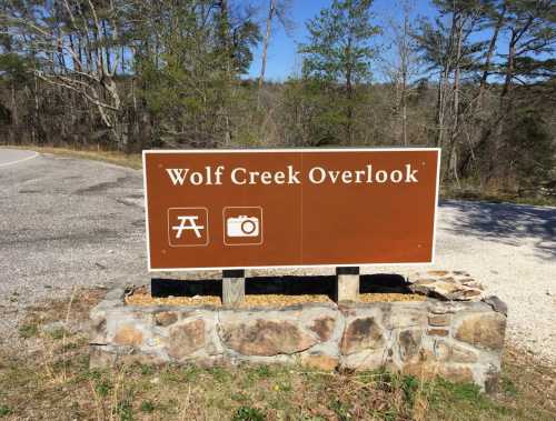 Sign for Wolf Creek Overlook featuring picnic and camera icons, surrounded by trees and a gravel road.