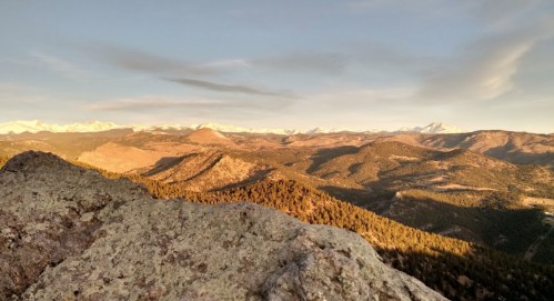 A panoramic view of mountains and valleys bathed in golden sunlight, with snow-capped peaks in the distance.