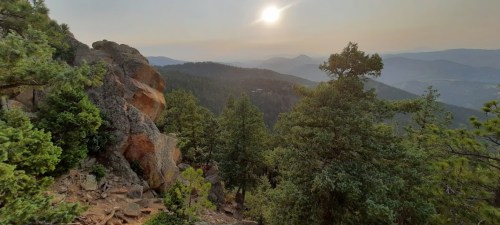 A scenic mountain view with trees in the foreground and a hazy sunset in the background.