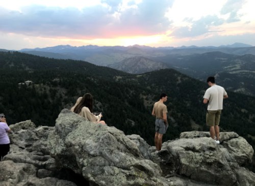 A group of people on rocky terrain overlooking a mountainous landscape at sunset.