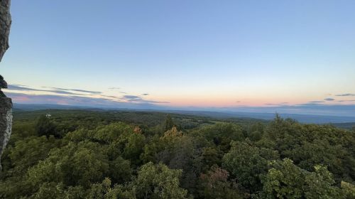 A panoramic view of rolling hills and trees under a pastel sky at dusk.