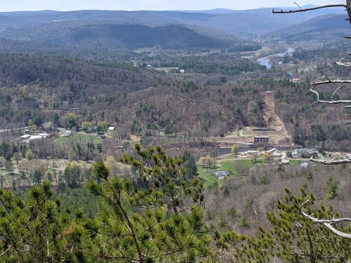 A panoramic view of a valley with rolling hills, trees, and a river, showcasing a mix of greenery and cleared land.