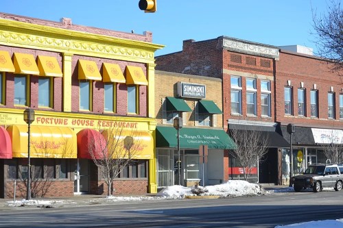 Colorful storefronts line a street, featuring a yellow restaurant and a brick building with a green awning. Snow is visible.