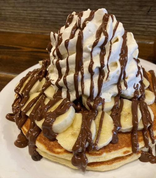 A stack of pancakes topped with sliced bananas, whipped cream, and drizzled chocolate sauce.