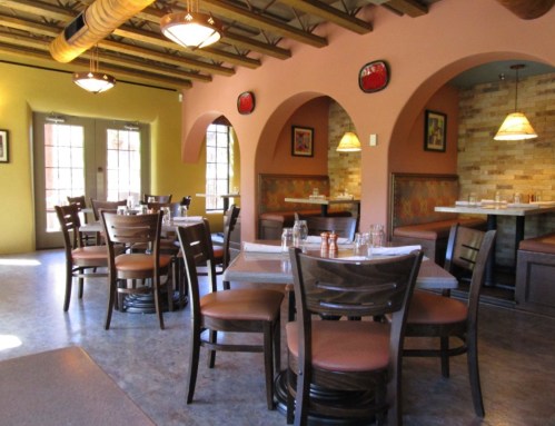 Cozy restaurant interior with wooden tables, chairs, and arched doorways, featuring warm colors and soft lighting.