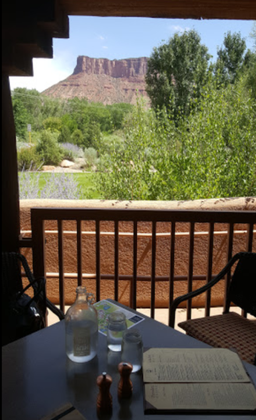 View from a patio table with a menu, featuring a scenic mountain backdrop and lush greenery.