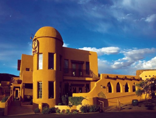 A southwestern-style building with a rounded dome, featuring adobe architecture and a blue sky with clouds.