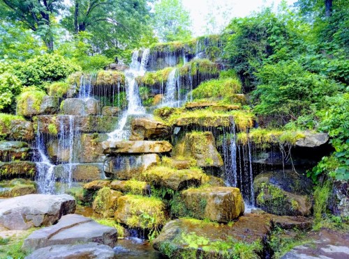A serene waterfall cascading over moss-covered rocks, surrounded by lush green foliage.