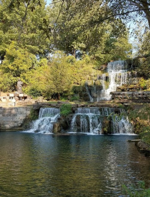 A serene waterfall cascading into a calm pool, surrounded by lush greenery and rocky formations.