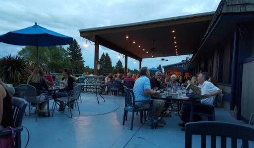 Outdoor dining area with tables, umbrellas, and people enjoying a meal during twilight.