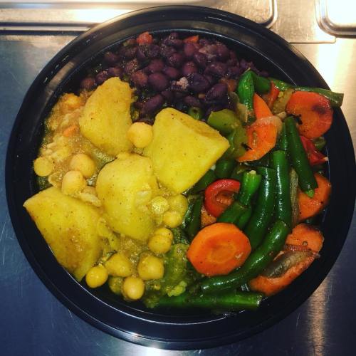 A black bowl filled with yellow potatoes, chickpeas, green beans, carrots, and black beans.