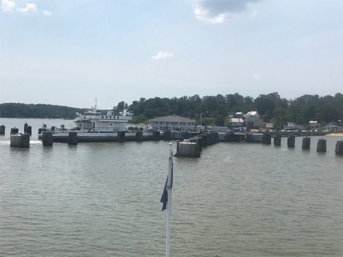 A ferry docked at a waterfront with piers and a small town in the background under a clear blue sky.