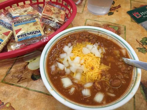 A bowl of chili topped with cheese and onions, alongside a basket of crackers on a festive tablecloth.