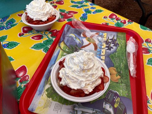Two bowls of strawberry dessert topped with whipped cream, placed on a colorful tablecloth with a magazine underneath.