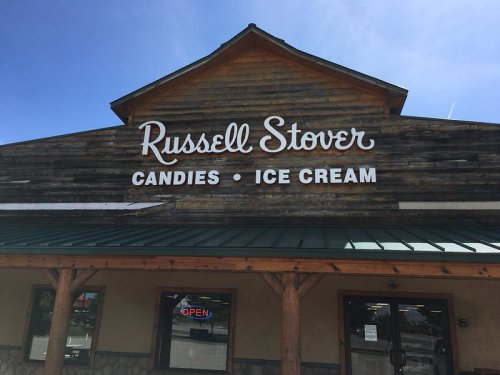 Sign for Russell Stover Candies and Ice Cream on a wooden building with a clear blue sky. "Open" sign visible.