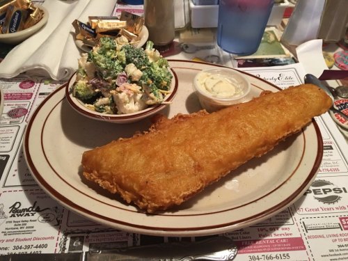 A plate with a golden fried fish fillet, a side of creamy coleslaw, and a small dish of dipping sauce.