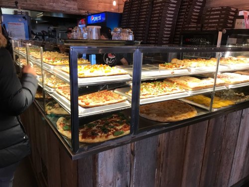 A display case filled with various types of pizza and baked goods in a casual eatery.