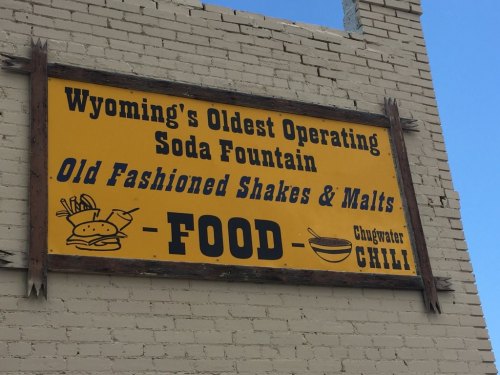 Sign for Wyoming's oldest operating soda fountain, featuring old-fashioned shakes and malts, with food and chili icons.