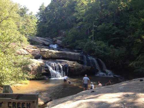 A serene waterfall cascades into a pool, surrounded by lush greenery and people enjoying the water.