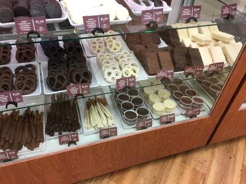 A display case filled with various chocolate treats, including cookies, fudge, and chocolate-covered snacks, with price tags.