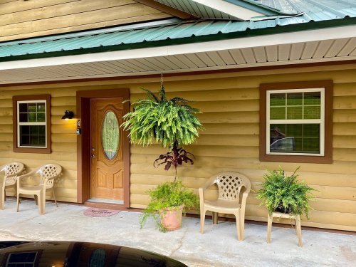 A cozy wooden cabin entrance with a brown door, potted plants, and two chairs on a concrete porch.