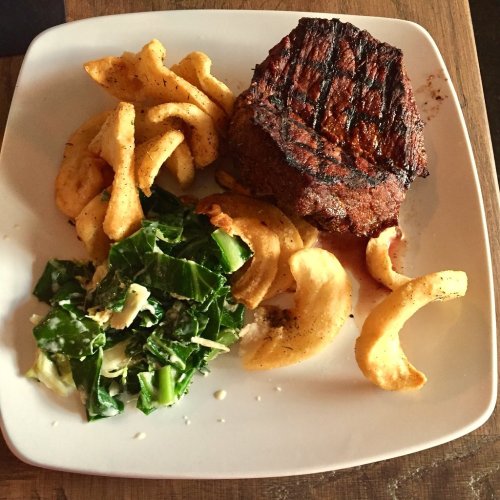 A plate featuring grilled steak, curly fries, and a side of greens.