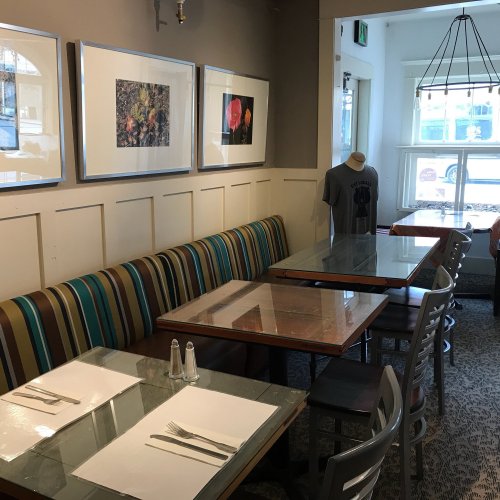A cozy restaurant interior with striped seating, glass tables, and framed flower art on the walls.