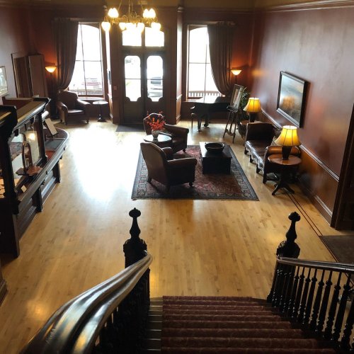 A spacious, elegantly furnished lobby with wooden floors, armchairs, and large windows letting in natural light.