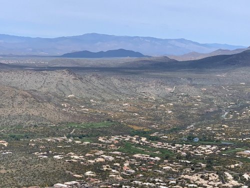 A panoramic view of a mountainous landscape with valleys and scattered homes under a clear blue sky.