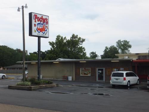 A restaurant building with a sign reading "Poches" and a parking lot, surrounded by trees under a cloudy sky.