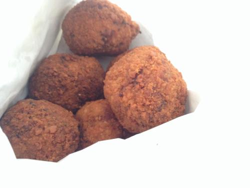 A close-up of several golden-brown, crispy fried balls in a white paper bag.
