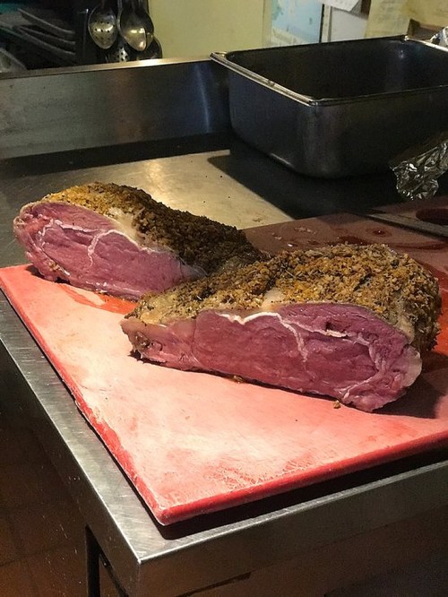 Two large cuts of seasoned meat resting on a red cutting board in a kitchen setting.