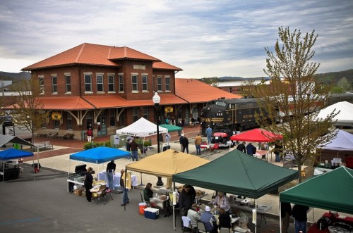 A bustling outdoor market with colorful tents near a historic train station and a vintage locomotive.