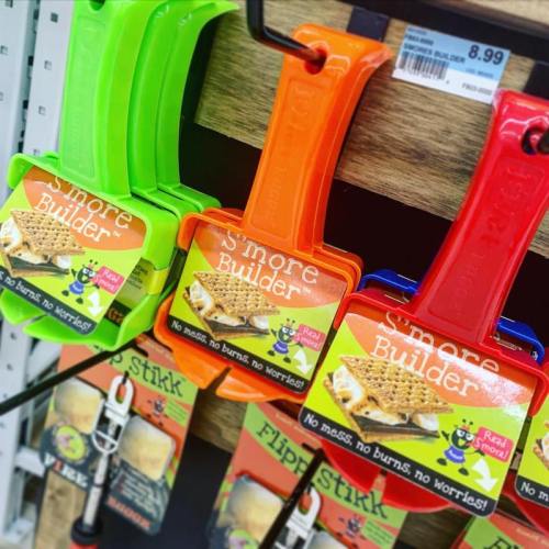 Two colorful s'more builder tools in green and red, hanging on a display with a price tag.