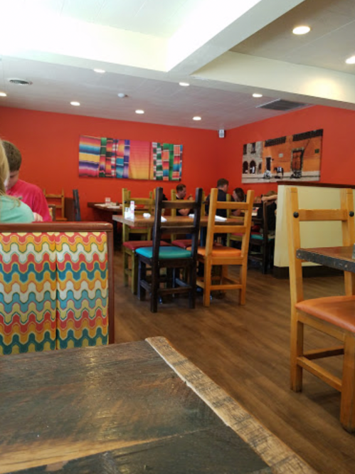 A cozy restaurant interior with colorful chairs, wooden tables, and vibrant orange walls. Customers are seated at tables.