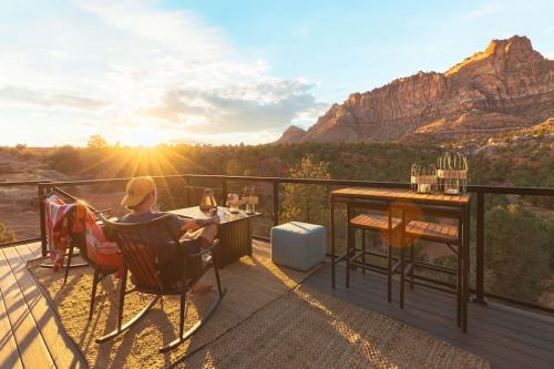 A person relaxes on a balcony with a stunning mountain view at sunset, surrounded by nature.