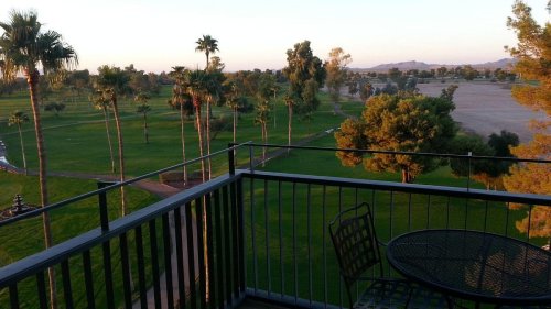 A balcony view overlooking a lush green golf course with palm trees and distant mountains under a clear sky.