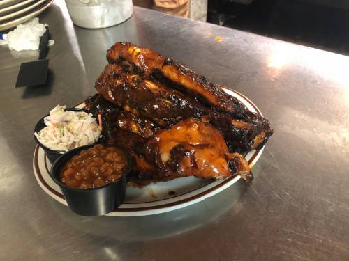 A plate of barbecue ribs, chicken, coleslaw, and baked beans on a metal surface.