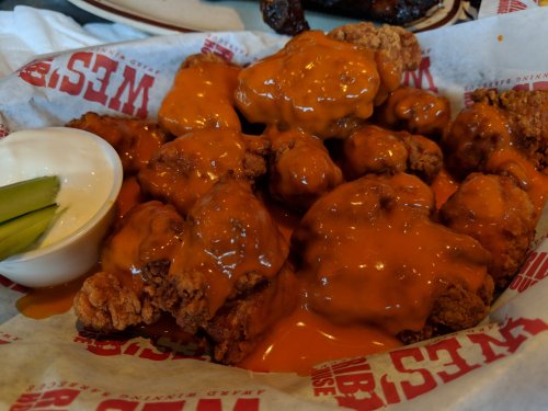 A basket of crispy fried chicken wings coated in orange sauce, served with a side of ranch dressing and celery sticks.