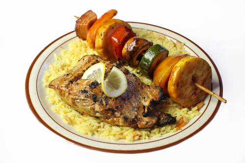 Grilled chicken with lemon on a bed of rice, accompanied by colorful vegetable skewers.