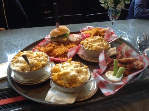 A tray of comfort food featuring mac and cheese, chicken wings, fries, a burger, and dipping sauces.