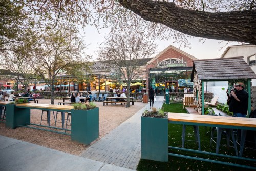 Outdoor dining area with tables and greenery, featuring a Hopdoddy restaurant and a cozy seating area.