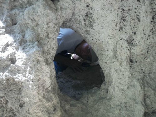 A person peeks through a circular hole in a rocky surface, holding an object in their hands.