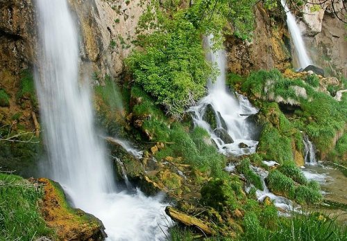 A serene landscape featuring cascading waterfalls surrounded by lush greenery and rocky terrain.