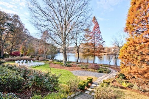 A serene lakeside view with a garden, chairs arranged for an event, and colorful trees in the background.