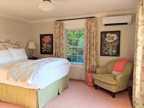 Cozy bedroom with a bed, floral curtains, armchair, and window overlooking greenery.