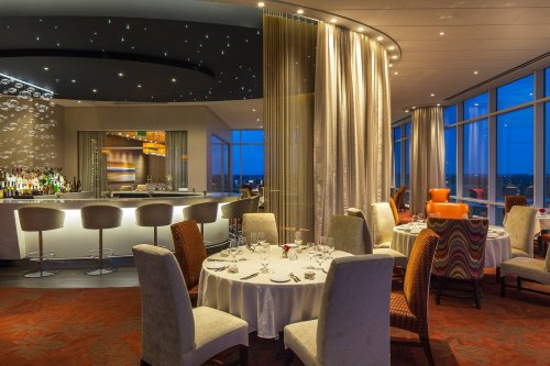 Elegant restaurant interior with modern decor, dim lighting, and a bar area, featuring tables set for dining.