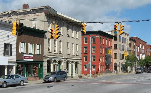 A street view featuring traffic lights, historic buildings, and parked cars in a small town setting.
