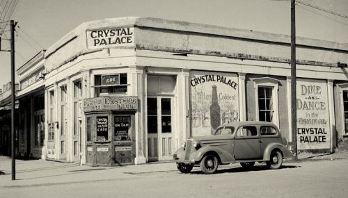 Historic black-and-white photo of the Crystal Palace building with vintage car parked outside.