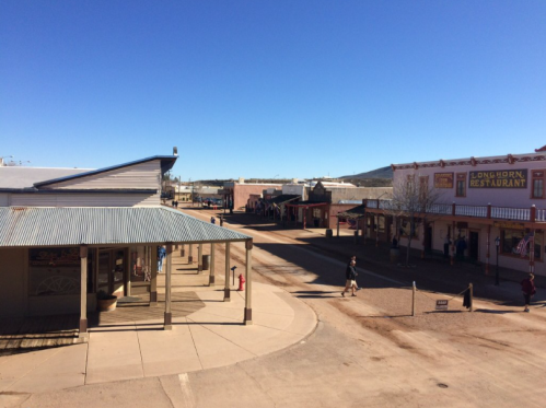 A sunny street view of a historic town with shops and a restaurant, under a clear blue sky.